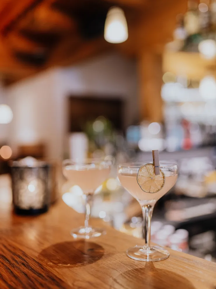 Zwei elegante Cocktails mit Limettengarnitur auf Holztheke bei gemütlicher Beleuchtung