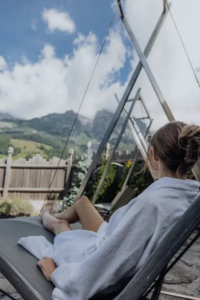 Frau entspannt im Bademantel auf Liege mit Bergblick im Outdoor-Spa-Resort
