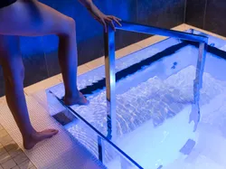 Person entering cold plunge pool using stainless steel handrail in spa setting