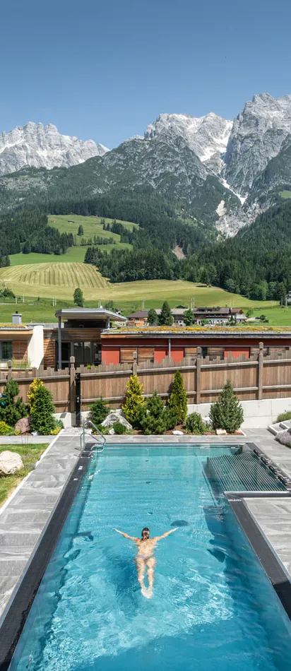 Bergresort mit Außenpool, Sonnenliegen und alpiner Landschaft im Hintergrund
