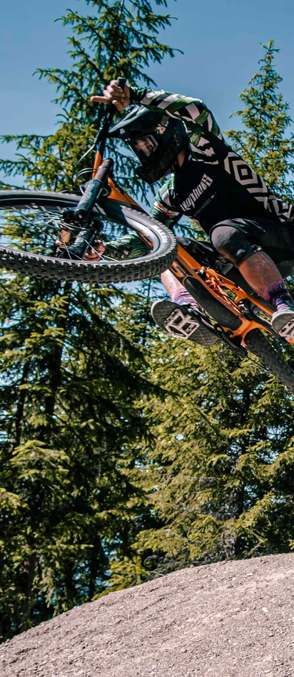 Mountainbiker springt in der Luft von einer Schanze im Waldtrail