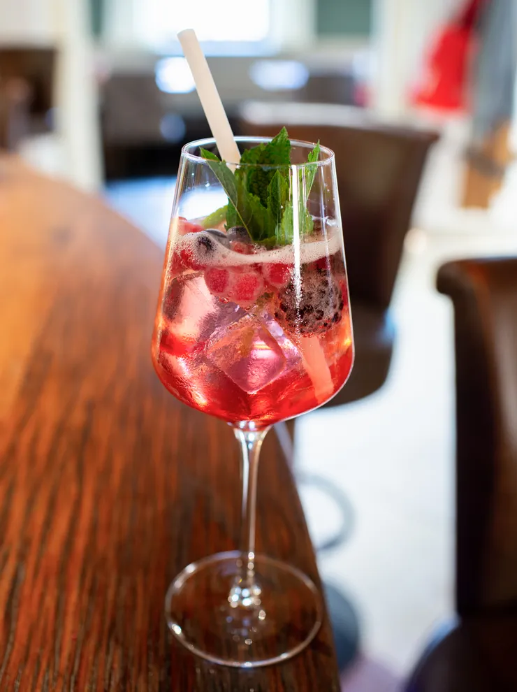 Refreshing berry cocktail with ice and mint in a wine glass on wooden bar