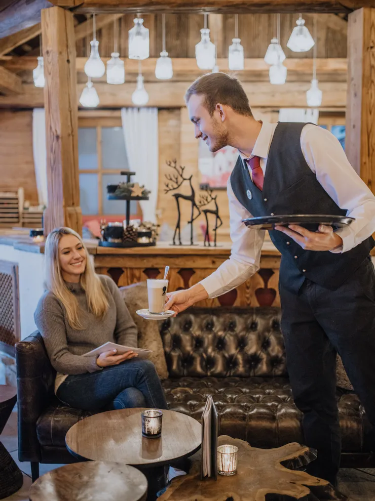 Waiter serving coffee to a smiling woman in a cozy rustic café