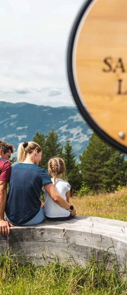 Familie auf Holzbank mit Blick auf die Berge in Saalfelden Leogang beim Wandern