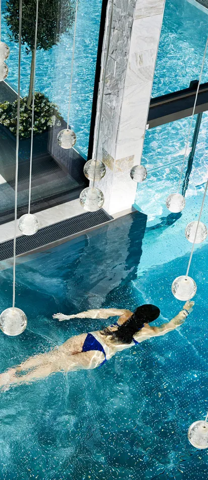 Frau schwimmt in einem luxuriösen Spa-Innenpool mit modernem Glasdesign