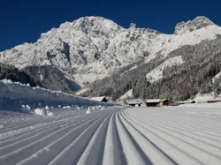 Groomed cross-country ski trail with snow-covered alpine mountains and cabins in background