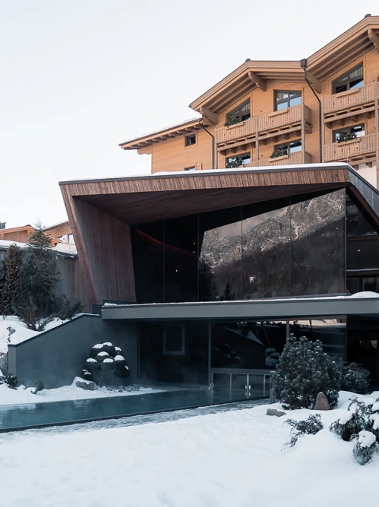 Modernes Alpenhotel mit Außenpool umgeben von Schnee in winterlicher Landschaft