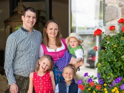 Happy family in traditional attire standing in front of Die Riederin hotel with flowers nearby