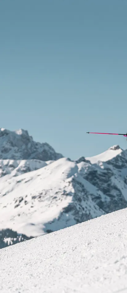 Gruppe Skifahrer auf verschneitem Hang mit Blick auf alpine Gipfel unter klarem blauen Himmel