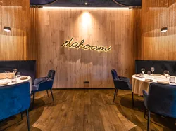 Elegant restaurant interior with round tables, blue velvet chairs and warm lighting, sign reads 'dahoam'