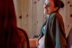 Smiling pregnant woman in bathrobe relaxing at spa and touching her belly