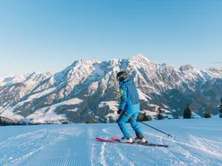 Skier in blue gear on groomed slope with snowy Alps mountain range in background