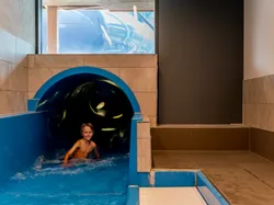 Lächelndes Kind kommt aus einer blauen Wasserrutsche in ein kleines Becken