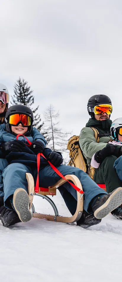 Family sledding down snowy slope with scenic winter mountain background