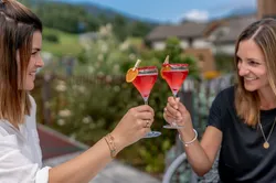 Two women clinking red cocktails garnished with orange slices outdoors