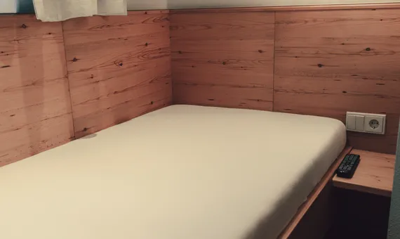 Minimalist single hotel bed with wooden paneling and soft wall light