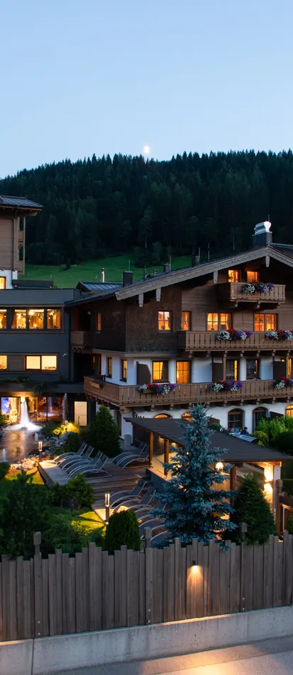 Beleuchtetes Alpenhotel mit Außenpool und Balkonen bei Sonnenuntergang