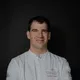 Male chef in white jacket with crossed arms and RIEDERALM logo on chest