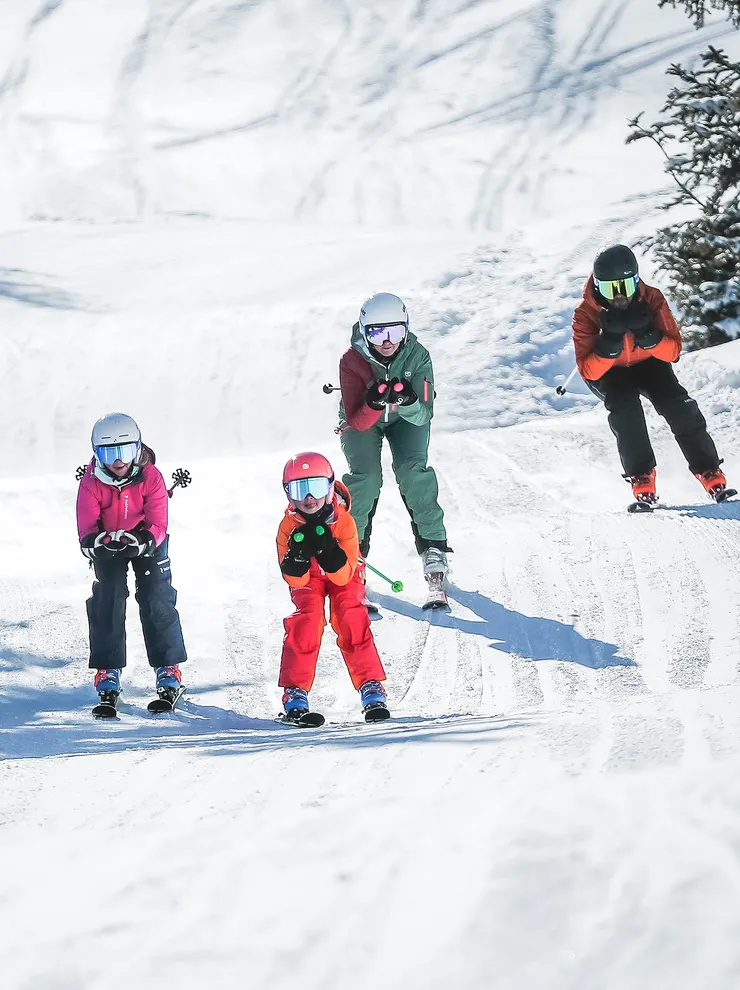 Familie fährt gemeinsam Ski auf einem verschneiten Berghang bei Sonnenschein