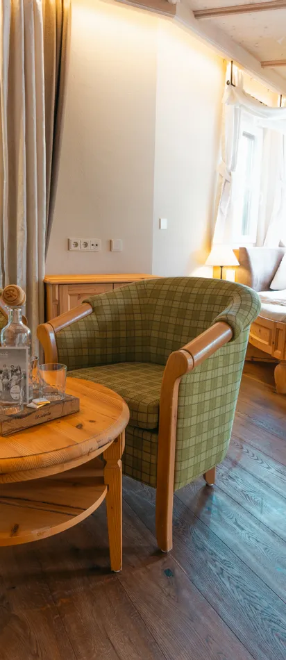 Gemütliches Hotelzimmer mit grünen Sesseln, rundem Holztisch und Himmelbett an hellen Fenstern