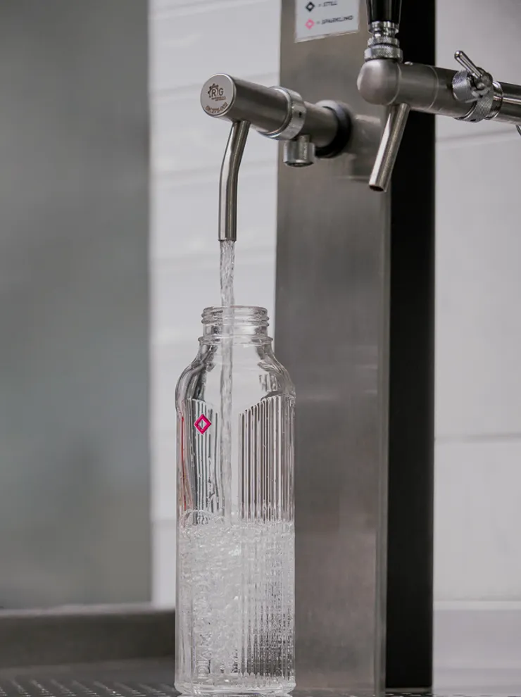 Glass water bottle being filled with still water from a modern water dispenser