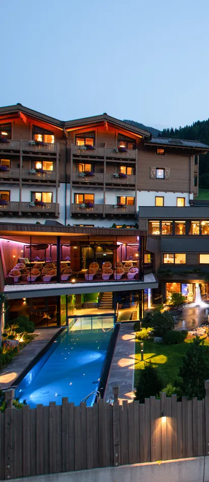 Beleuchtetes Alpenhotel mit Außenpool und Balkonen bei Sonnenuntergang