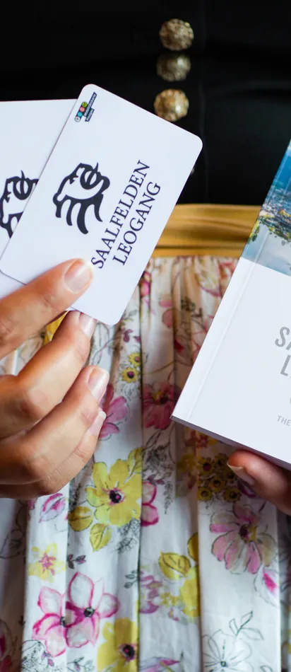 Woman in traditional dress holding Saalfelden Leogang Card and brochure for 2024–2025