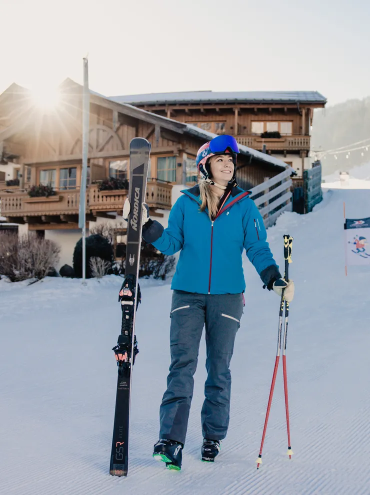 Frau in Skikleidung mit Skiern vor Chalet im sonnigen Skigebiet