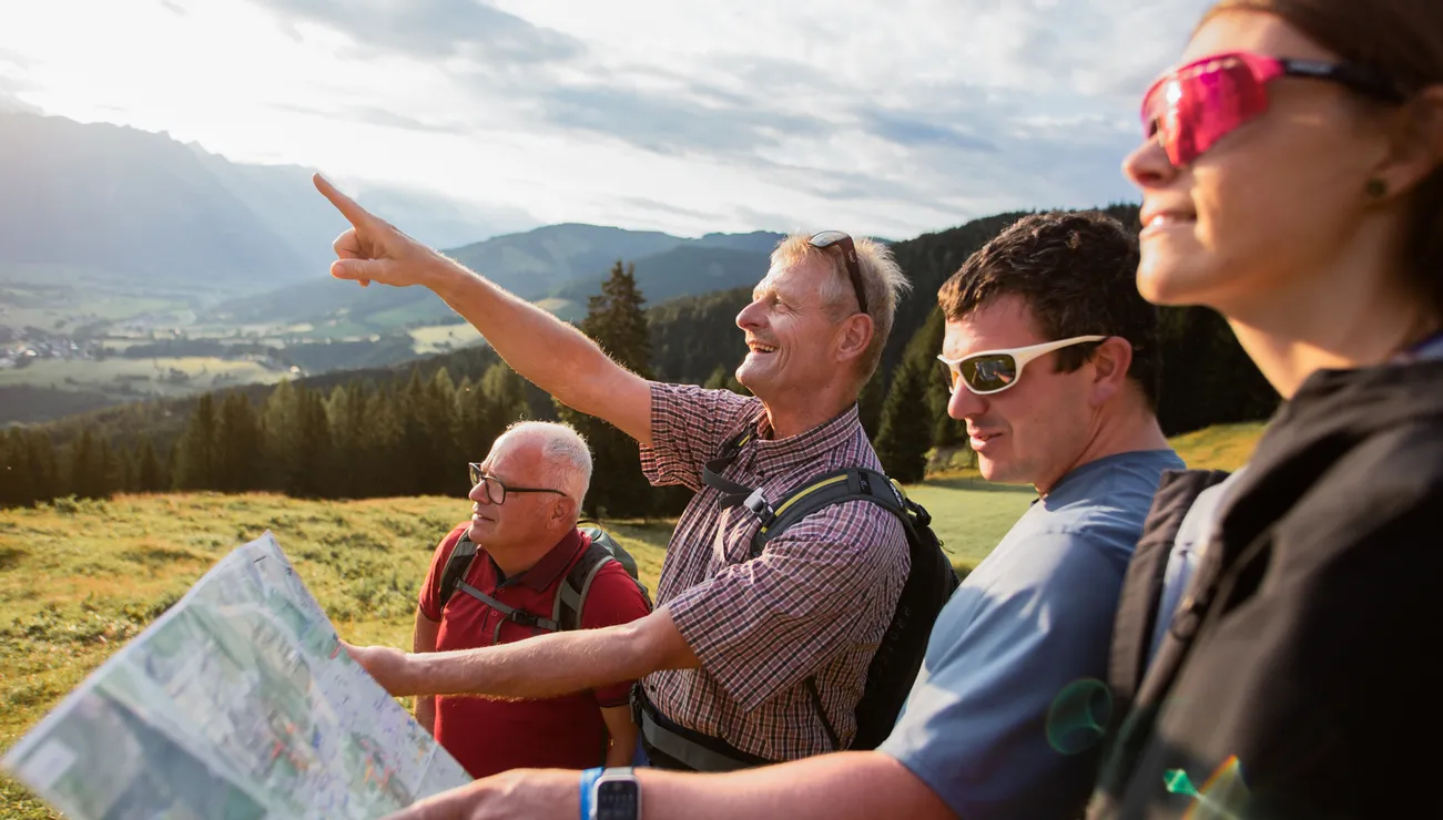 Wandergruppe liest Karte und zeigt auf Berge in alpiner Landschaft