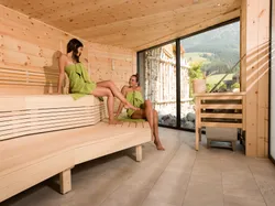 Two women relaxing in a modern wooden sauna with mountain view