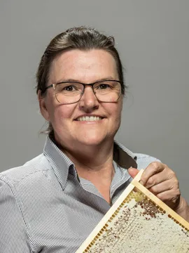 Smiling woman holding a honeycomb frame filled with fresh honey