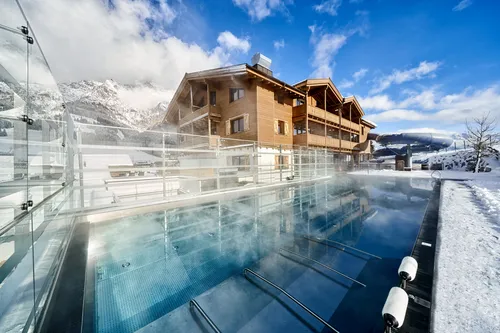 Beheizter Außenpool im Skigebiet mit Holzchalet und verschneiter Bergkulisse