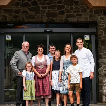 Mehrgenerationenfamilie posiert vor einem Wellnesshotel mit steinerner Fassade