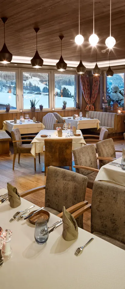 Elegantes Alpenrestaurant mit gedeckten Tischen und großen Fenstern mit Blick auf verschneite Berge