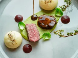 Gourmet beef dish with sauce, mashed potato domes, puree, and Brussels sprouts on elegant plate