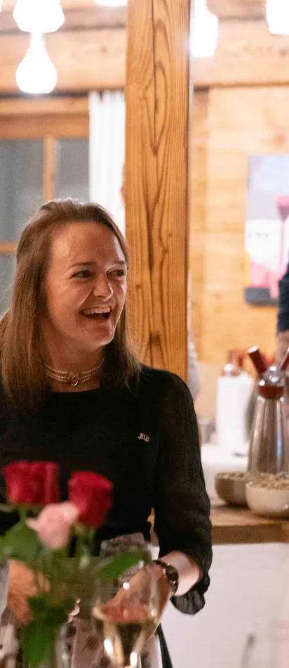 Three women laughing during a festive dinner in a cozy wooden restaurant