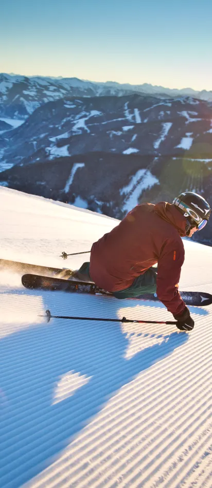 Skier carving on freshly groomed slope with mountain panorama at sunrise