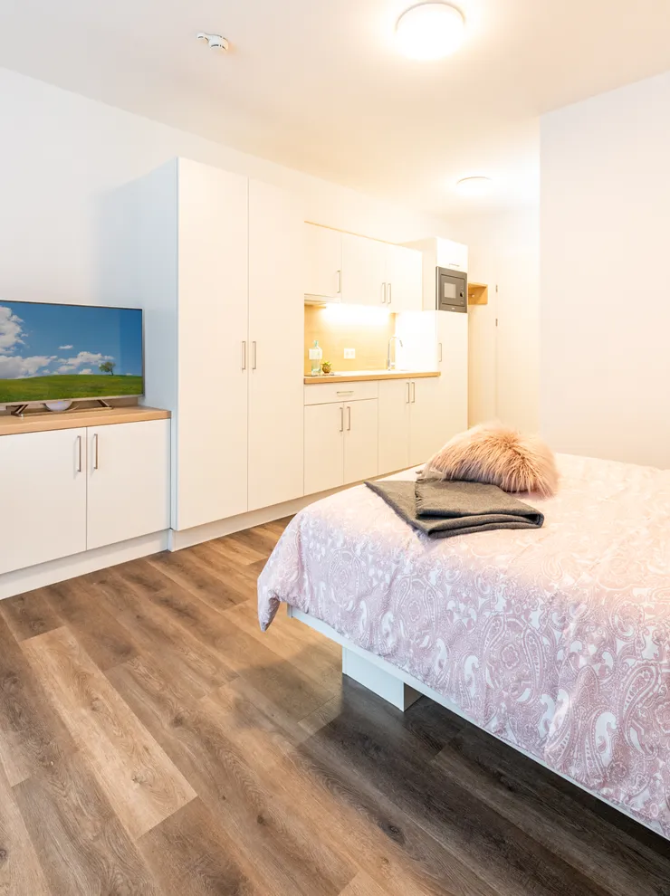 Modernes Studio-Apartment mit Küche, Bett, Fernseher und Essbereich auf Holzfußboden