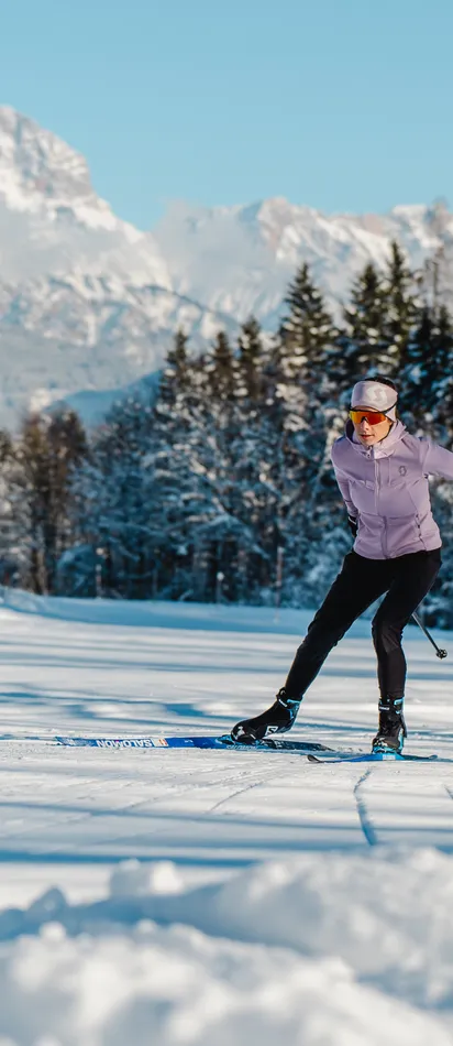 Woman cross-country skiing on a snowy trail with alpine mountains in the background