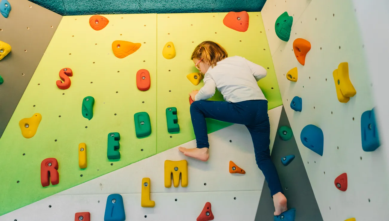 Kind klettert an Indoor-Boulderwand mit bunten Griffen in Buchstabenform