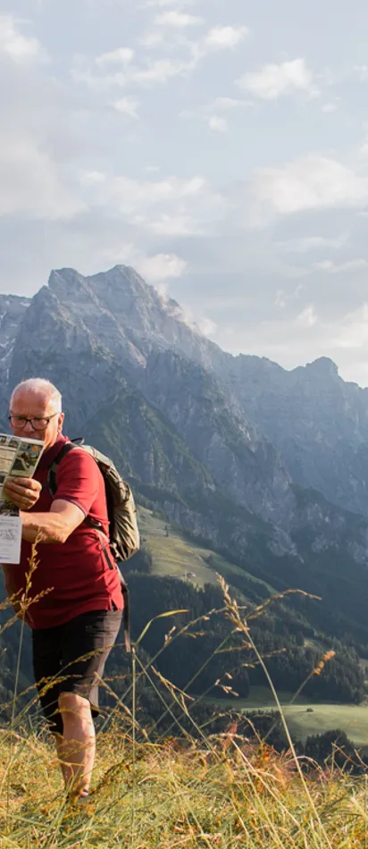 Gruppe von Wanderern betrachtet Karte auf Almwiese mit Alpenhintergrund