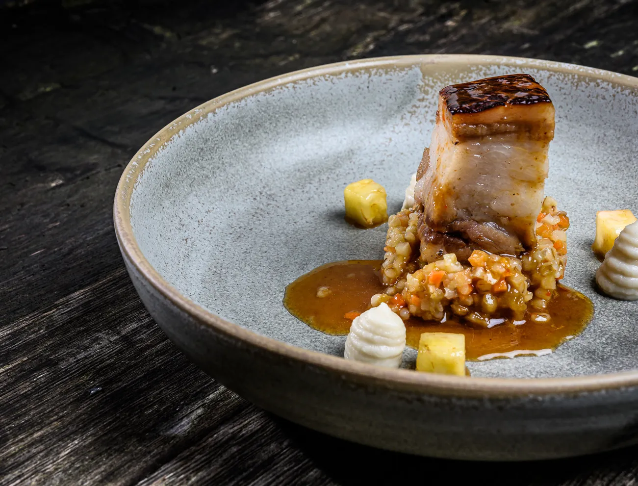 Gourmet-Schweinebauch mit Gerstenrisotto, Soße und Gemüse auf Keramikteller