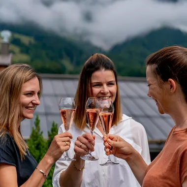 Frauen stoßen mit Rosé-Champagner auf einer Terrasse mit Bergblick an