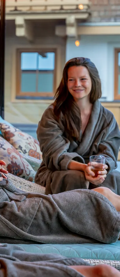 Three women relaxing in spa lounge chairs wearing robes and holding tea