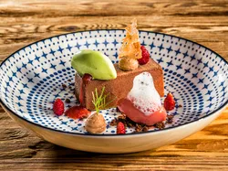 Gourmet-Schokoladendessert mit Erdbeersauce, grünem Sorbet und Schaum auf dekorativem Teller