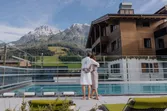 Paar in Bademänteln am Pool mit Blick auf die Alpen und ein Wellnesshotel