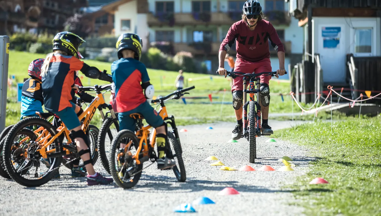 Mountainbike-Trainer unterrichtet Kinder bei einem Fahrtechniktraining im Freien