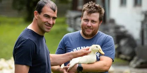 Zwei Männer auf einem Bauernhof halten gemeinsam eine junge Ente