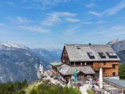 Mountain hut with outdoor terrace overlooking alpine valley and peaks under blue sky