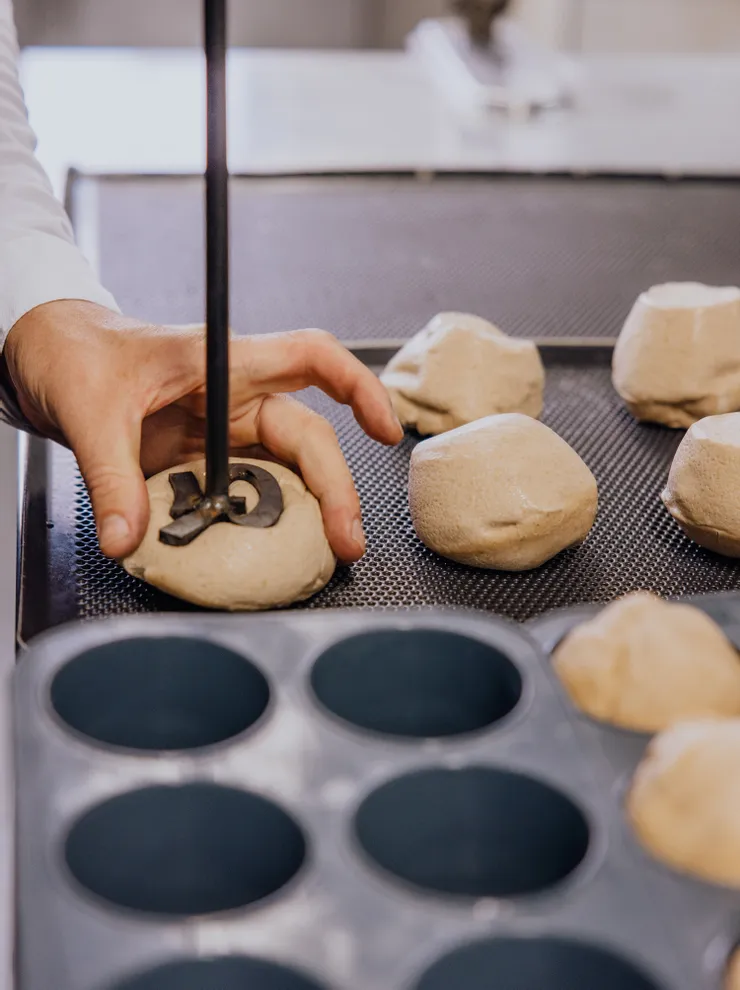 Baker pressing stamp into round bread dough before baking